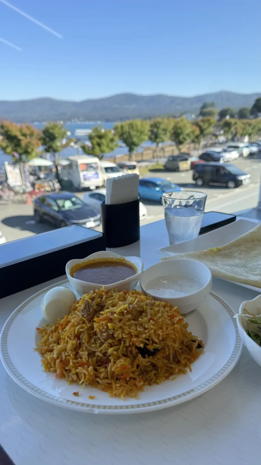 A plate of biryani by a window, with the lake, trees and hills outside under a blue sky