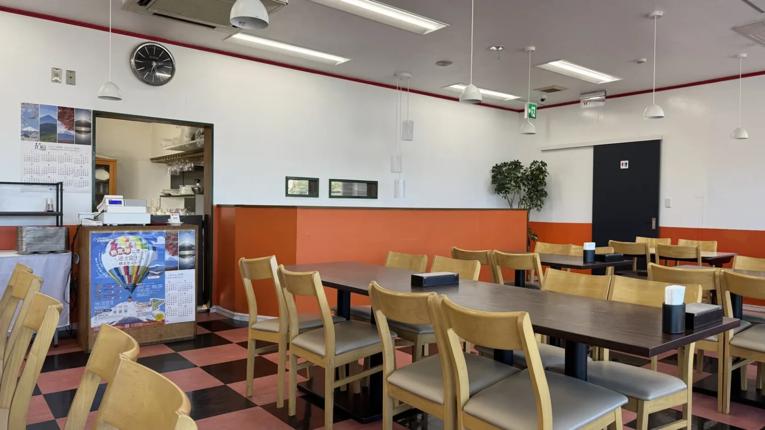 A dining room with wooden tables and chairs, an orange wall band and a red and black checked floor