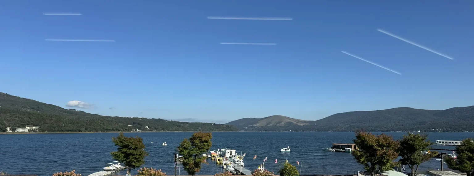 Lake Yamanaka under a blue sky, seen from the restaurant window, with boats at a pier and green hills