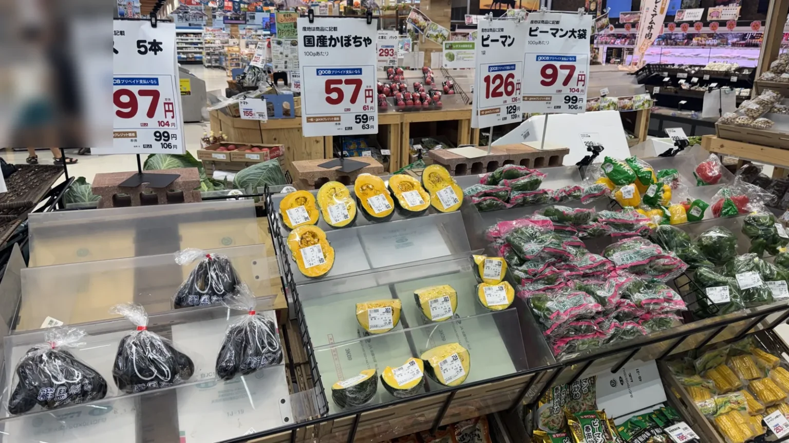 Vegetable displays with large red price signs, aubergines in bags, pumpkins and green peppers