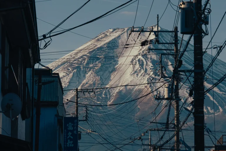 The snow-covered upper slopes of Mt Fuji rise behind a tangle of power lines and the edges of low buildings in Fujiyoshida on a clear February morning.