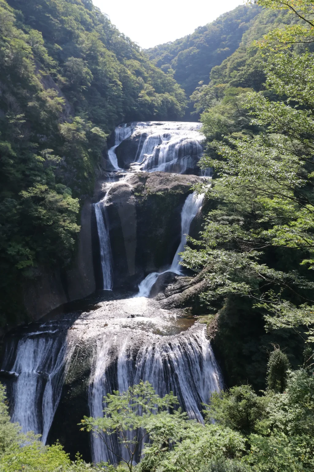 A waterfall falling in several steps through a narrow wooded gorge, seen from high above