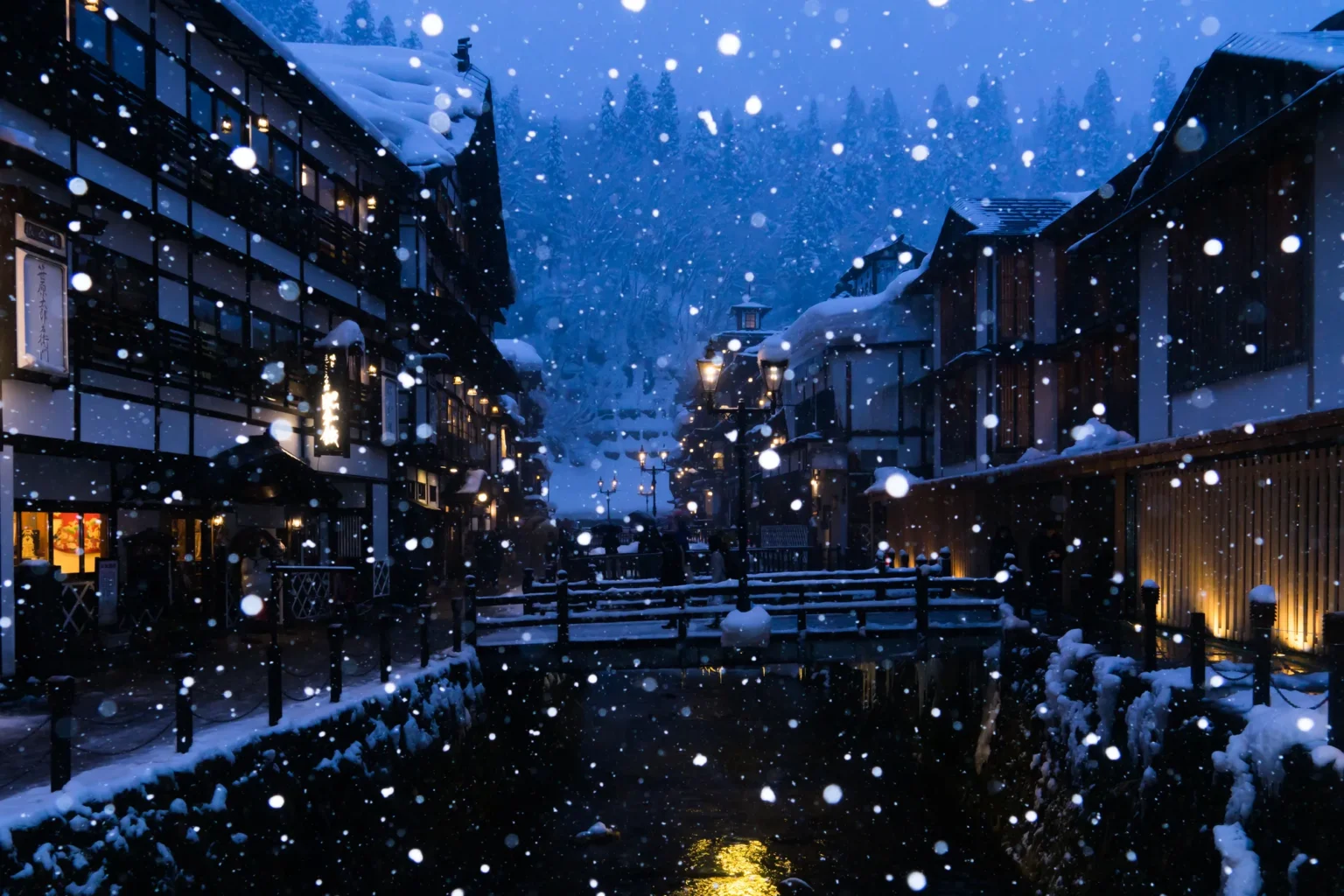 Ginzan Onsen at blue hour in falling snow, wooden inns lining both banks of the river