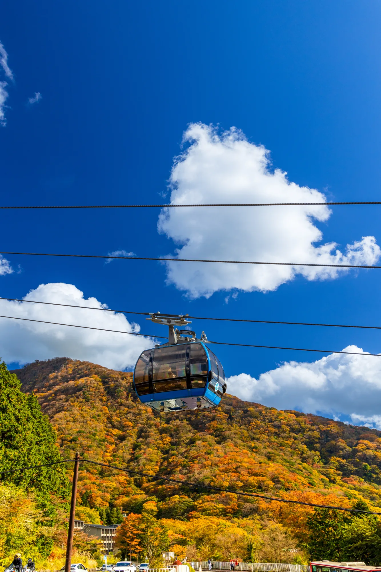 A Hakone Ropeway gondola passing autumn-coloured hills under a blue sky
