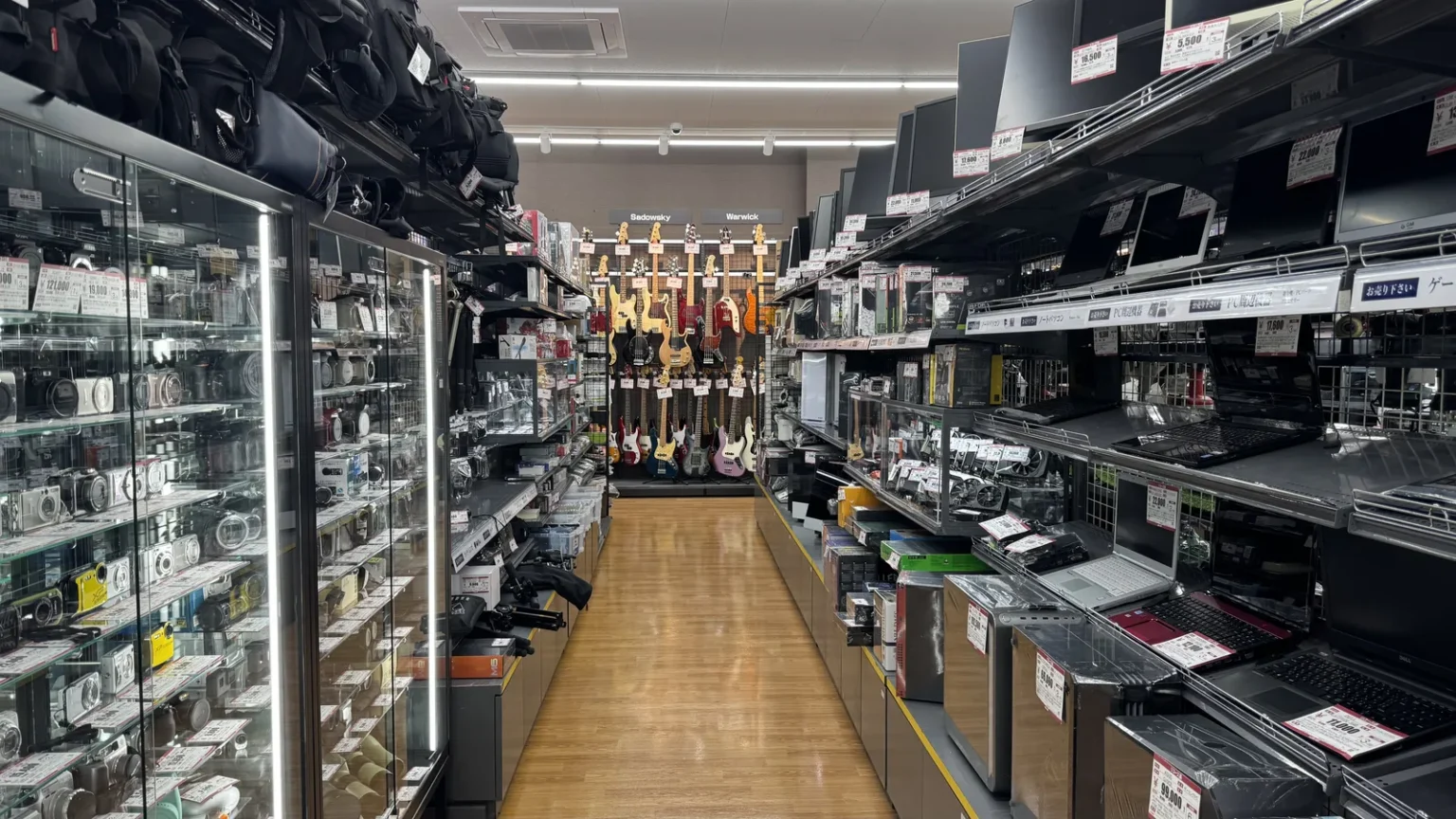 A narrow aisle between lit glass display cases, with shelves of goods on the right