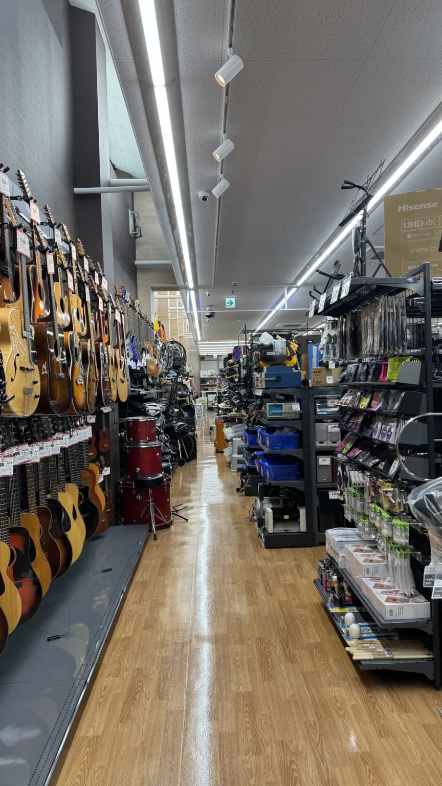 An aisle with guitars hanging along the left wall and shelves of goods on the right