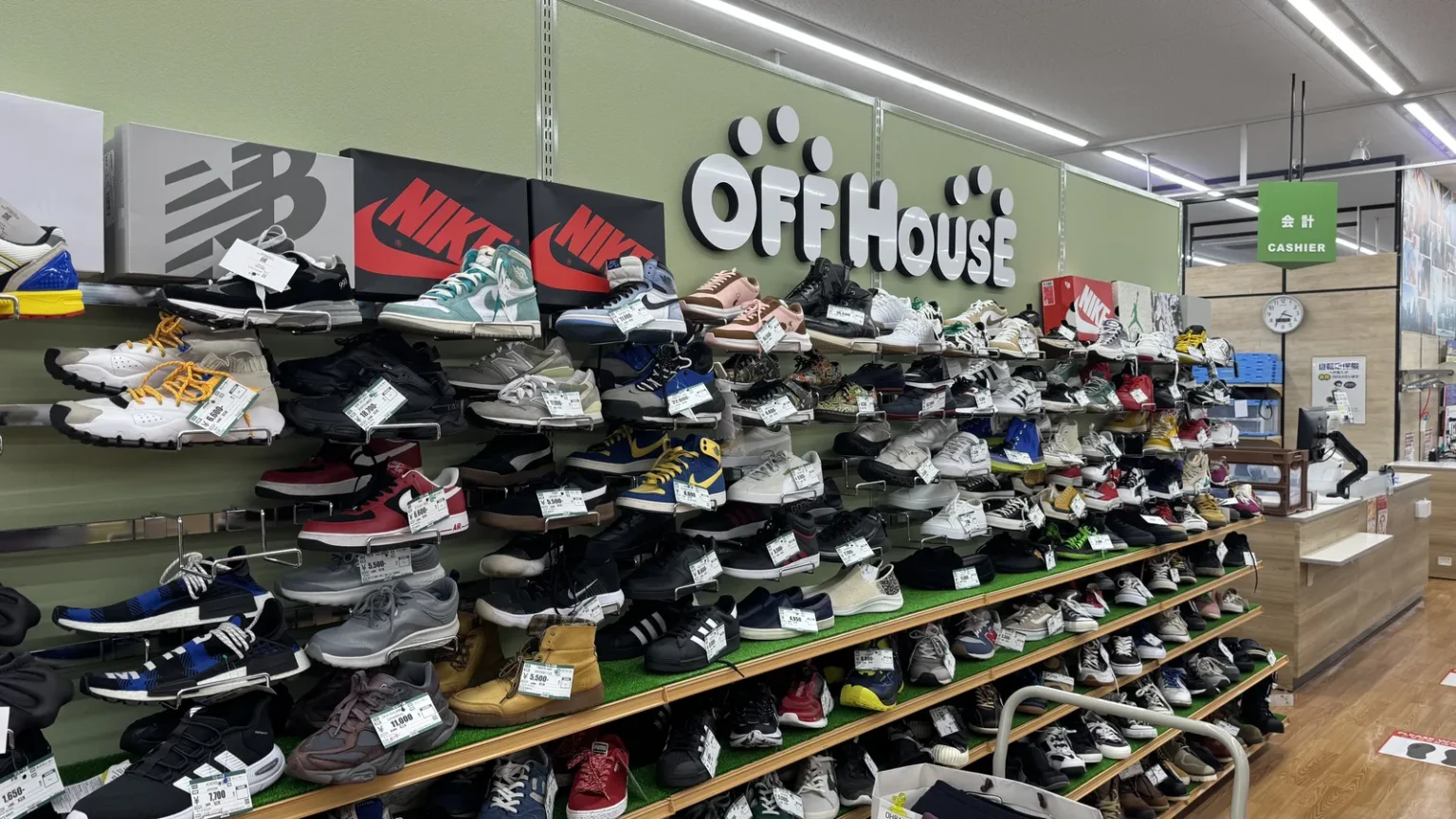 A wall of used sneakers on shelves under an Off House sign, with brand boxes on the top shelf