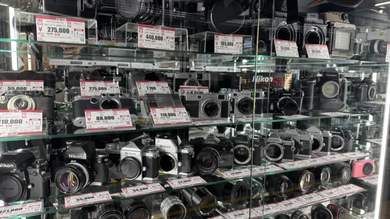 Glass shelves full of used film and digital cameras and lenses, each with a red and white price tag