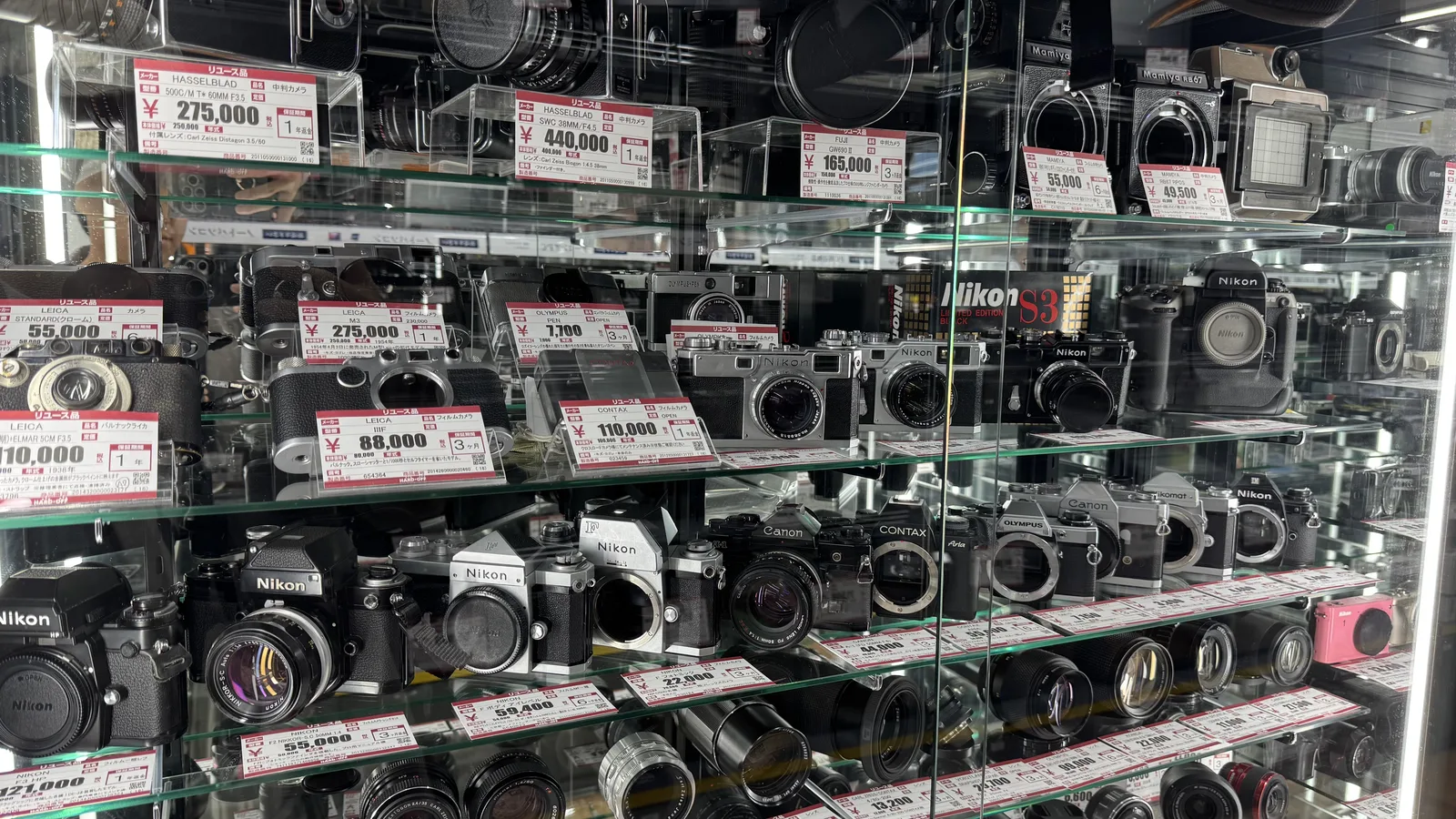 Glass shelves full of used film and digital cameras and lenses, each with a red and white price tag