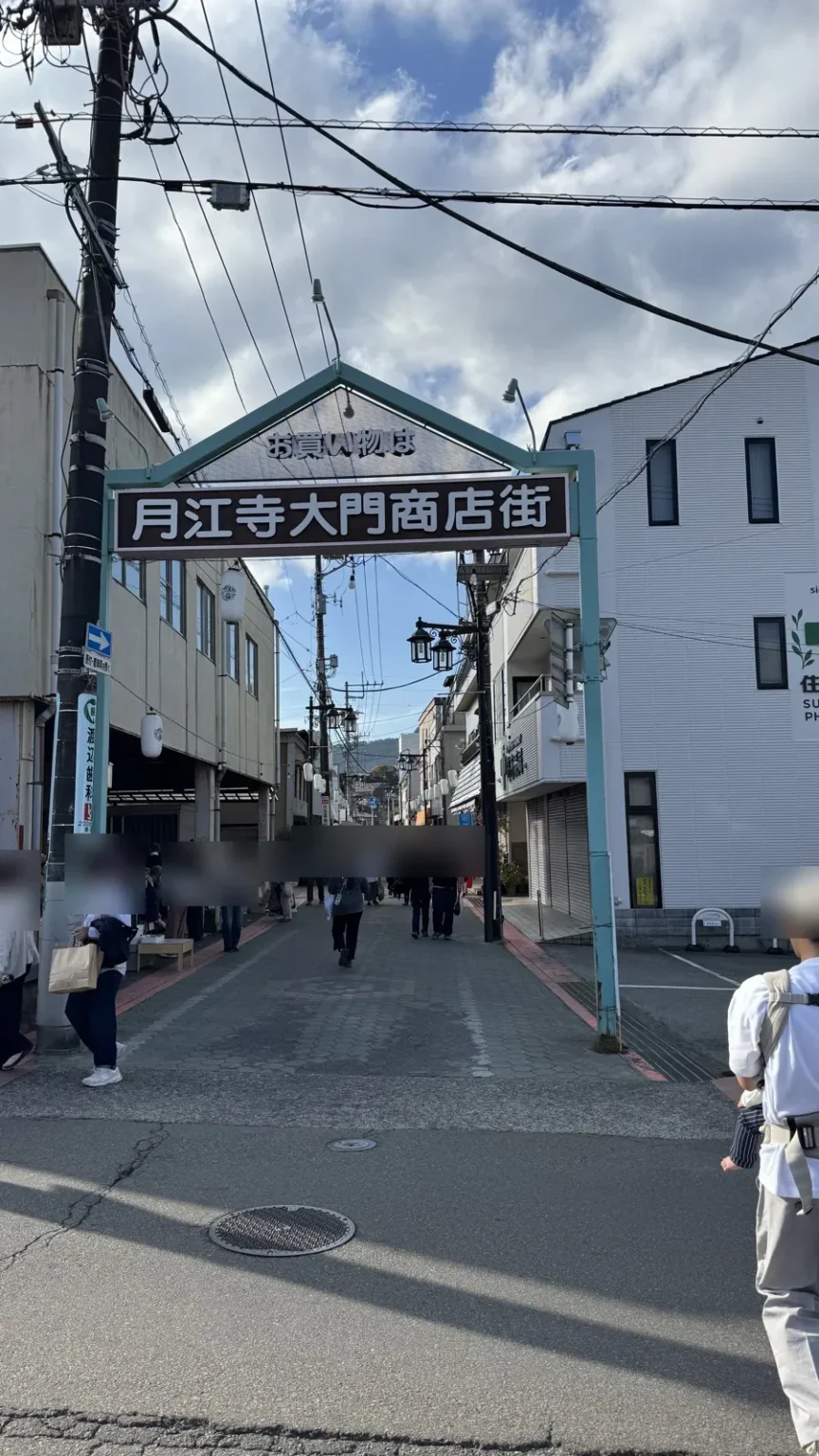The arched gate of the Gekkoji Daimon shopping street with its Japanese sign, and people walking down the narrow street of low shops beyond it