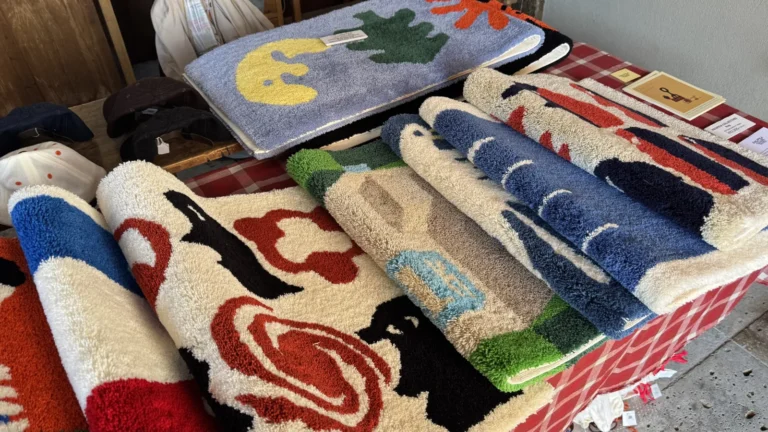 A stack of thick tufted mats in red, blue, white and green with bold graphic patterns on a stall table