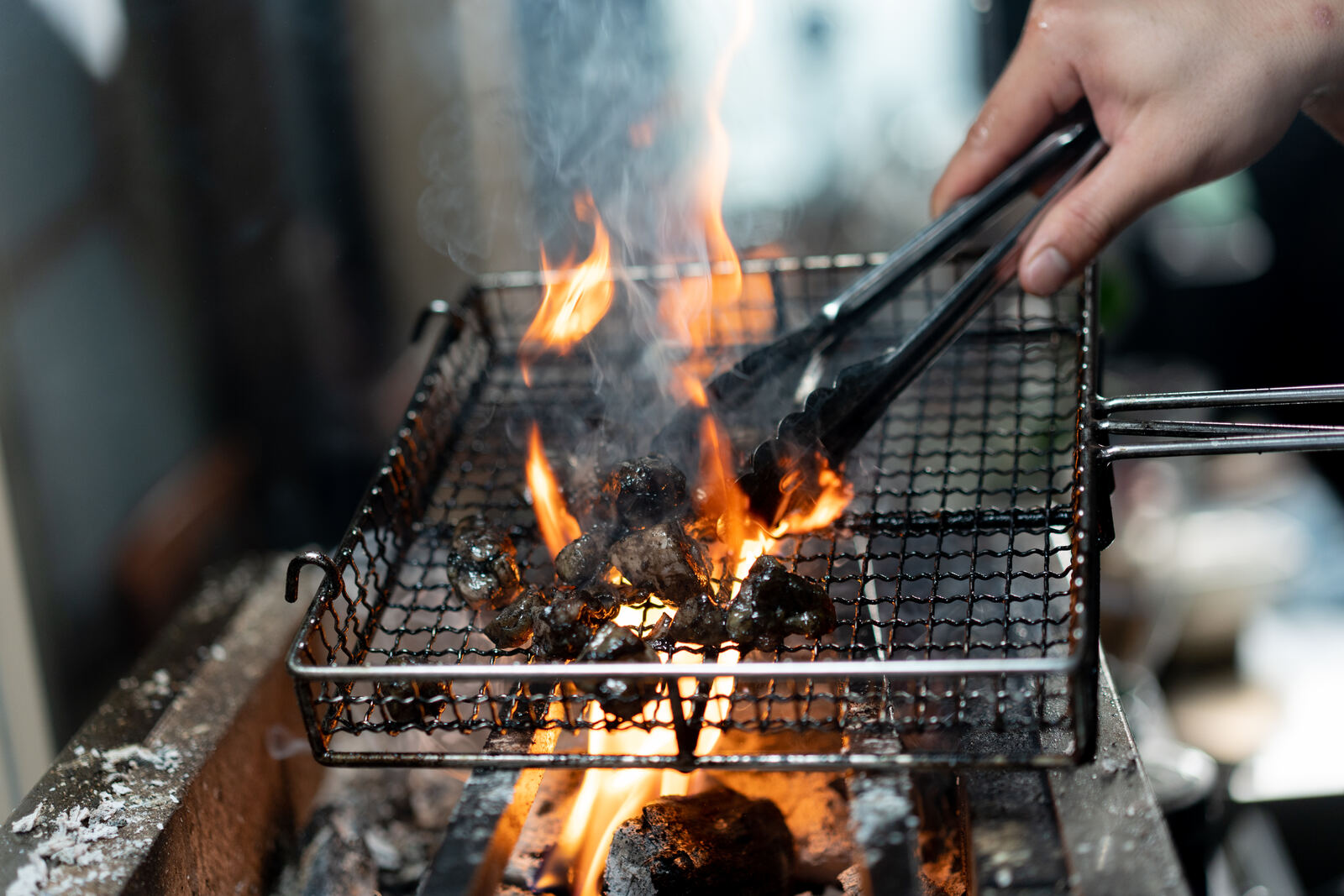 Chicken pieces on a wire grill over open charcoal flame, turned with tongs