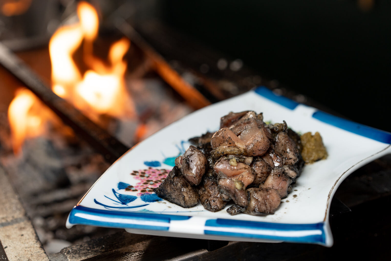 A plate of charcoal-grilled chicken pieces beside the grill