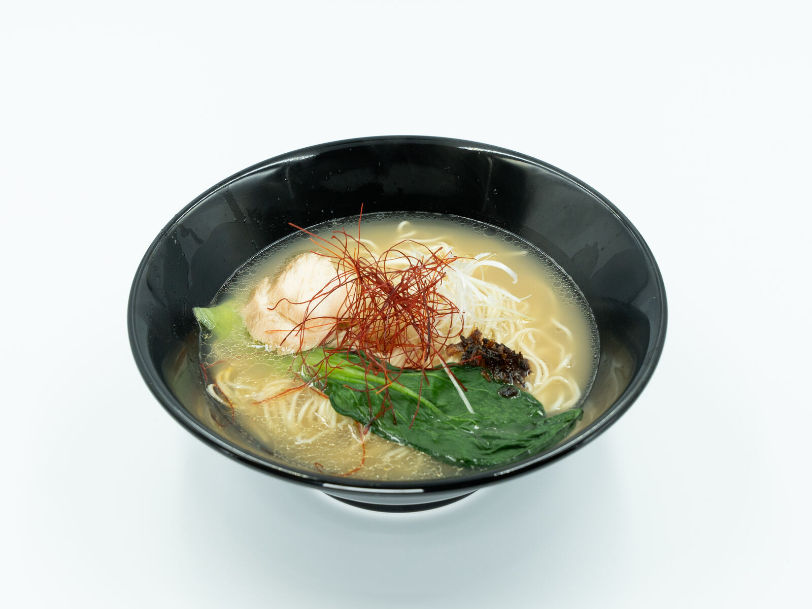 A black bowl of creamy chicken ramen topped with red chilli threads and greens