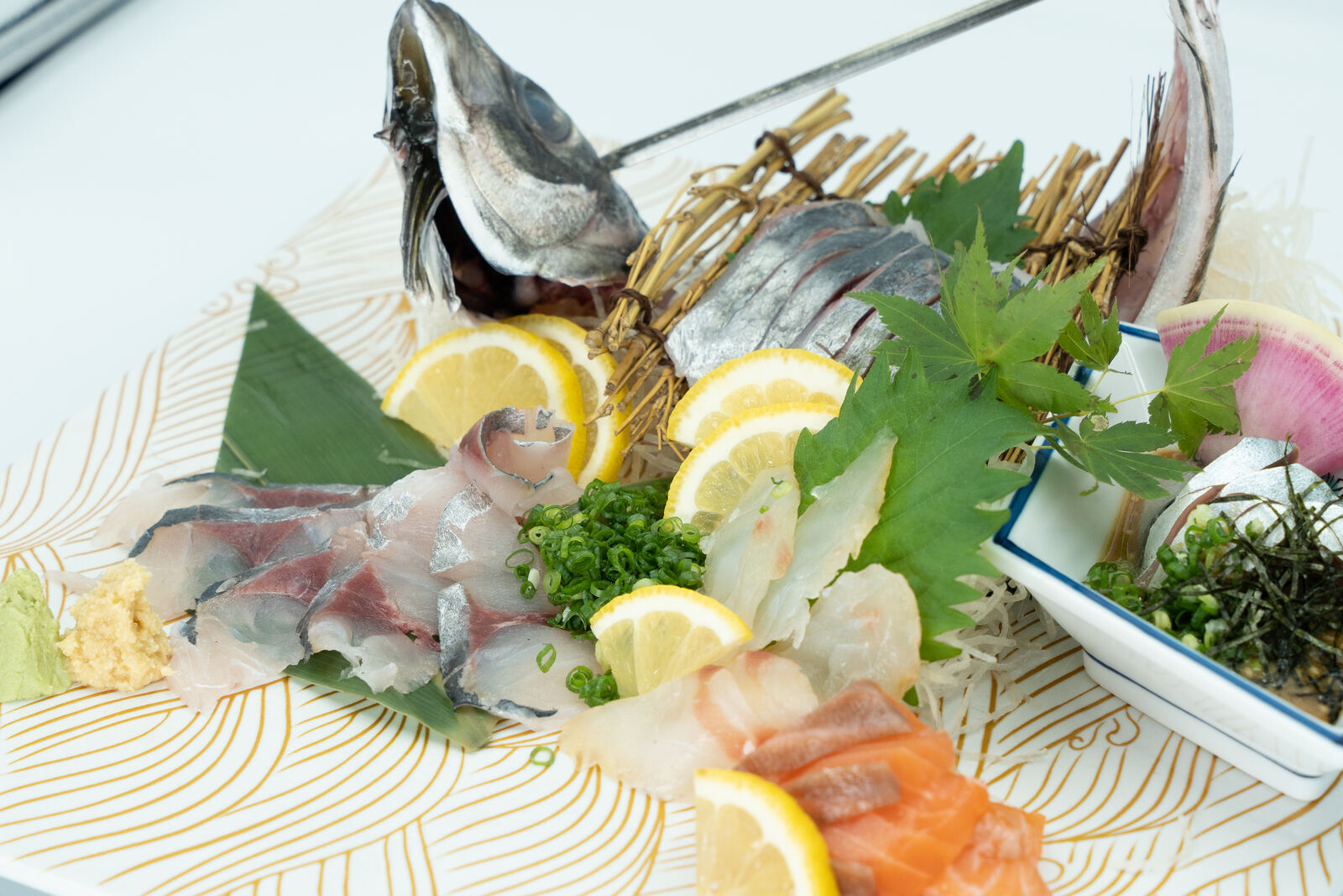 A sashimi platter with whole fish head, lemon and shiso leaves
