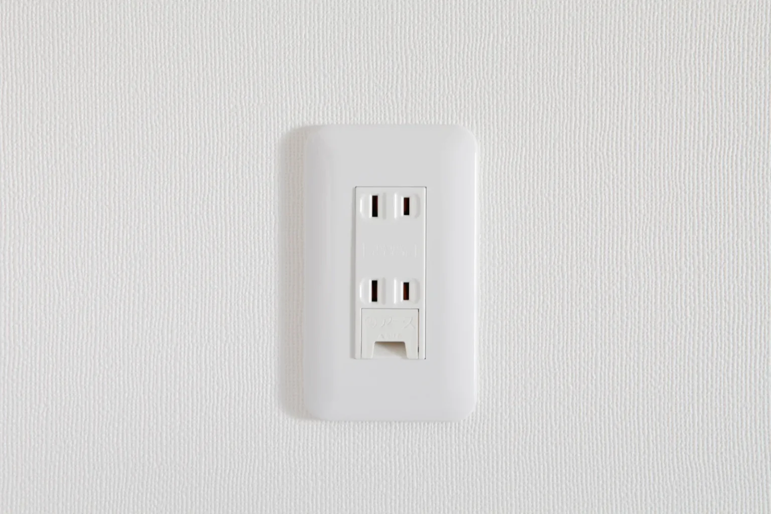 A white wall outlet with two two-slot sockets and, below them, a small covered terminal labelled アース (earth) in Japanese