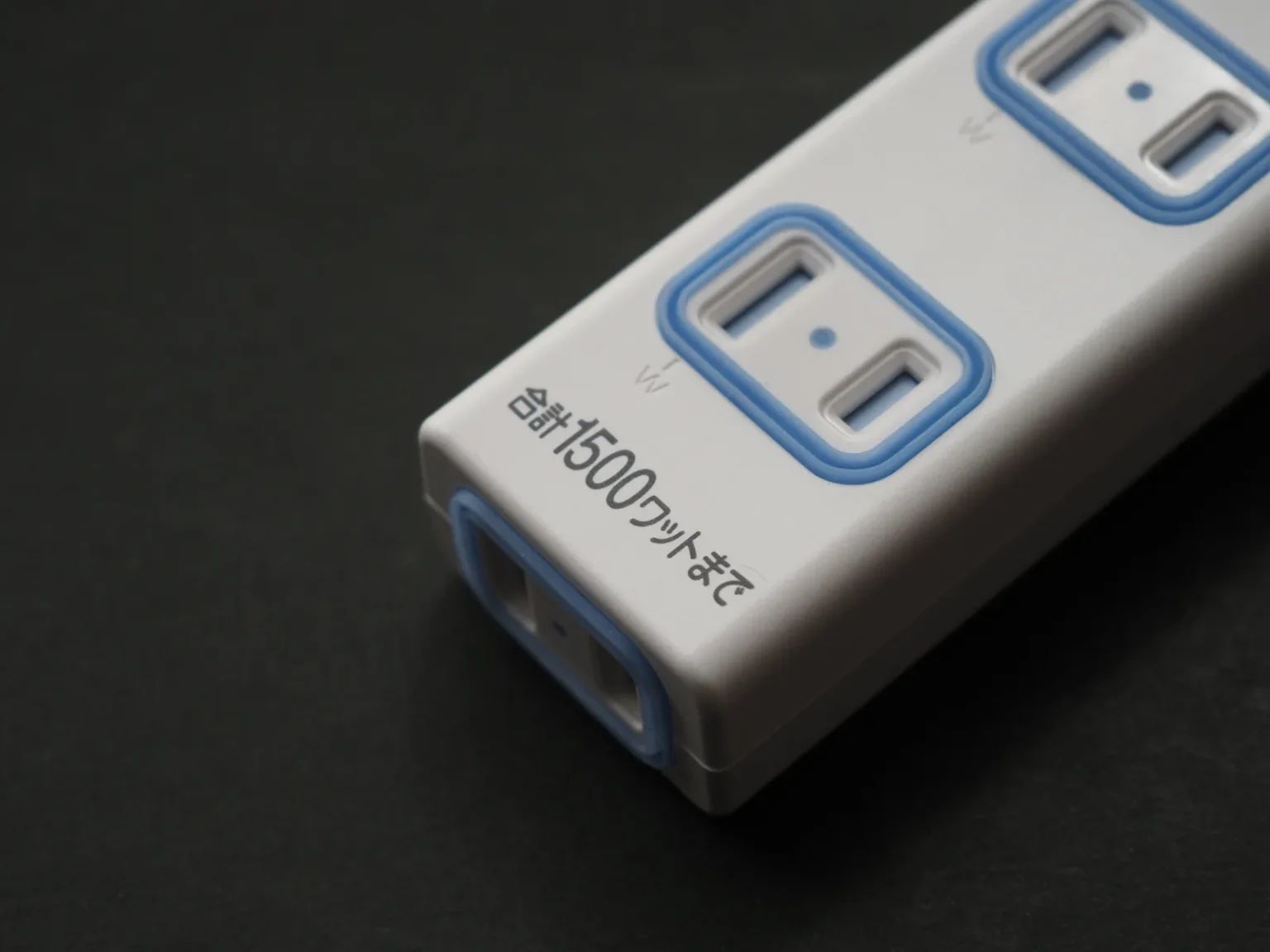 Close-up of a white Japanese power strip with blue-rimmed two-slot sockets and the printed words 合計1500ワットまで