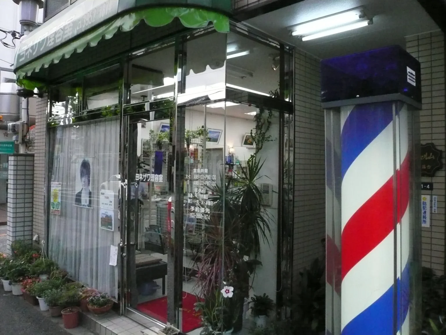 A small barbershop front in Tokyo with a red, white and blue barber pole by the door