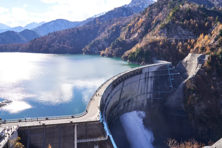 Kurobe Dam releasing water below its reservoir, with autumn colour on the surrounding mountains, Tateyama Kurobe Alpine Route