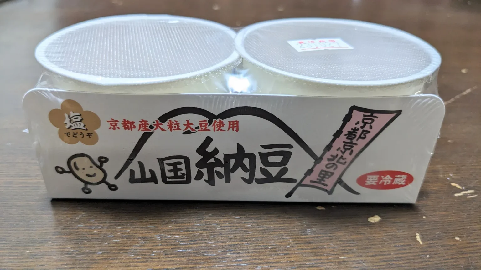 A two-pack of round natto tubs in a paper sleeve printed 山国納豆, Yamaguni natto, with a cartoon soybean, a drawing of mountains, a flower-shaped label reading 塩でどうぞ, with salt, please, and a note that the beans are large Kyoto-grown soybeans.