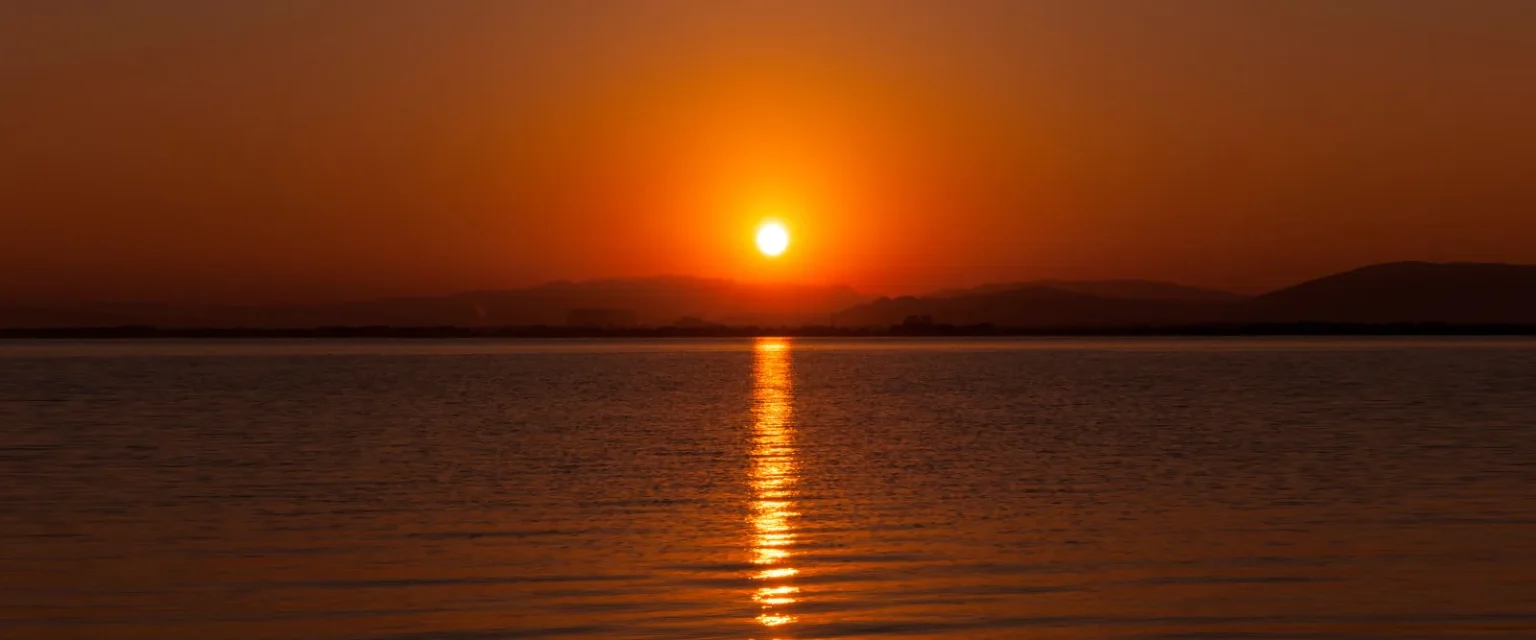 The sun low above the far shore of Lake Biwa, with an orange sky and a line of light across calm water