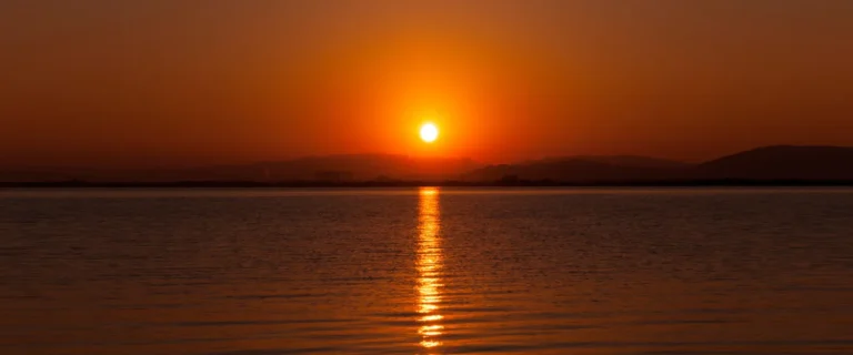 The sun low above the far shore of Lake Biwa, with an orange sky and a line of light across calm water
