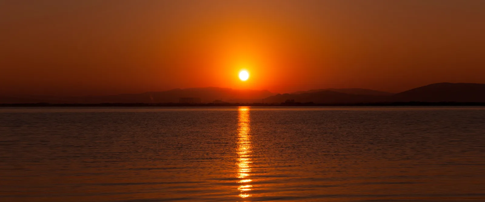 The sun low above the far shore of Lake Biwa, with an orange sky and a line of light across calm water