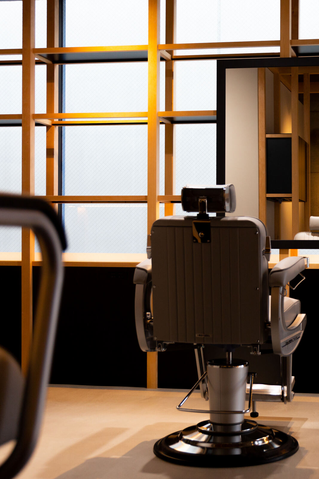 A single styling chair seen from behind, facing a wood-framed window