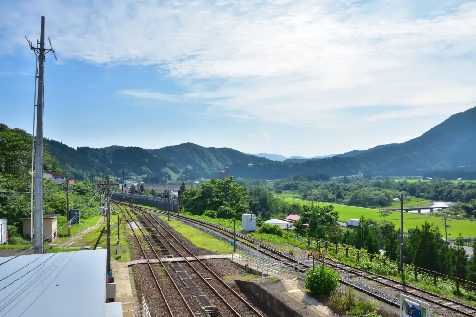 Railway tracks at JR Naruko-Onsen Station seen from above, with green hills and a river in the distance