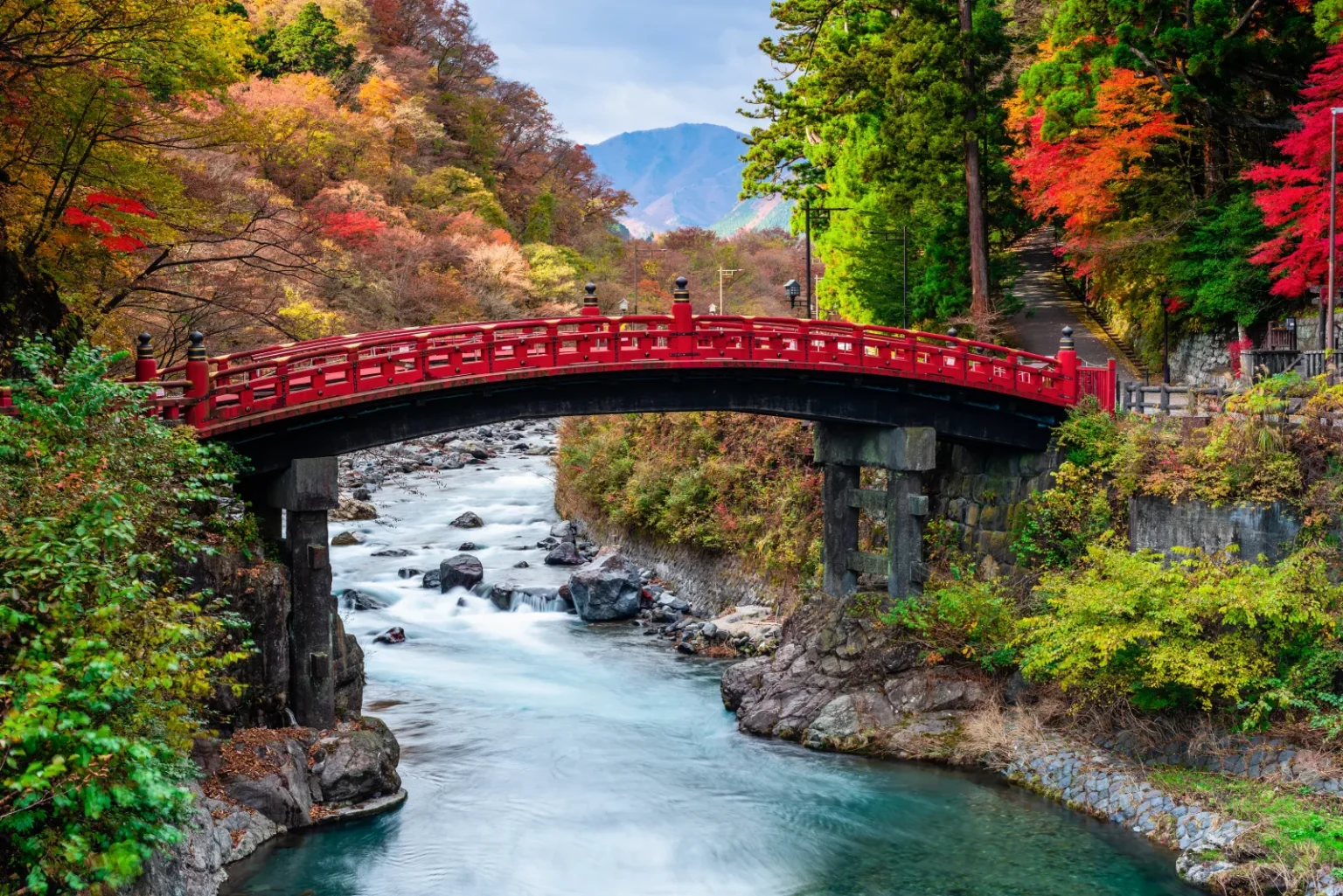 The red-lacquered Shinkyo bridge spanning the rocky Daiya River with red and yellow trees on the banks