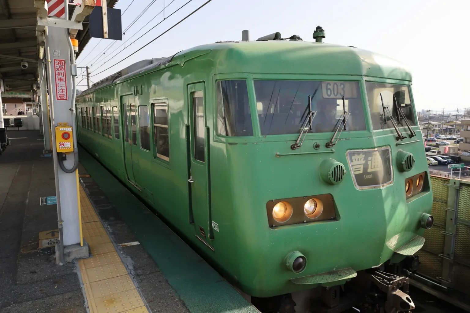 A green JR West local train stopped at a platform on the Kosei Line
