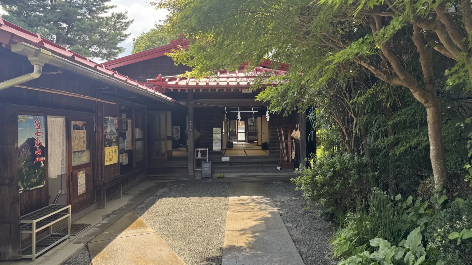A long gravel path leading between wooden buildings with red roofs to the open entrance of the house