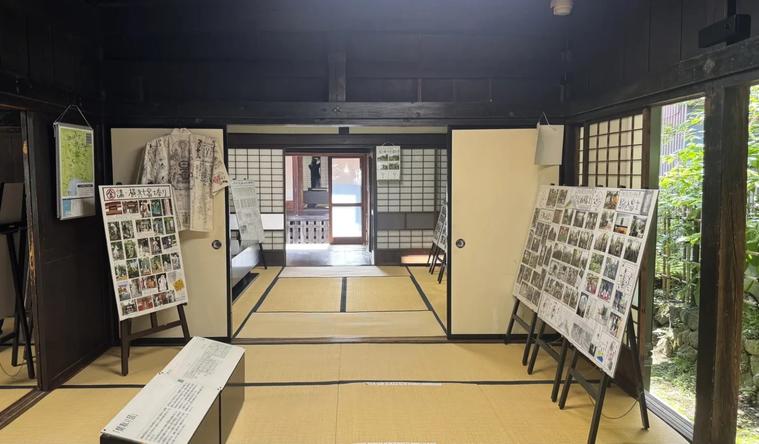 A tatami room with display boards of photos and text on stands, opening through sliding doors into further rooms