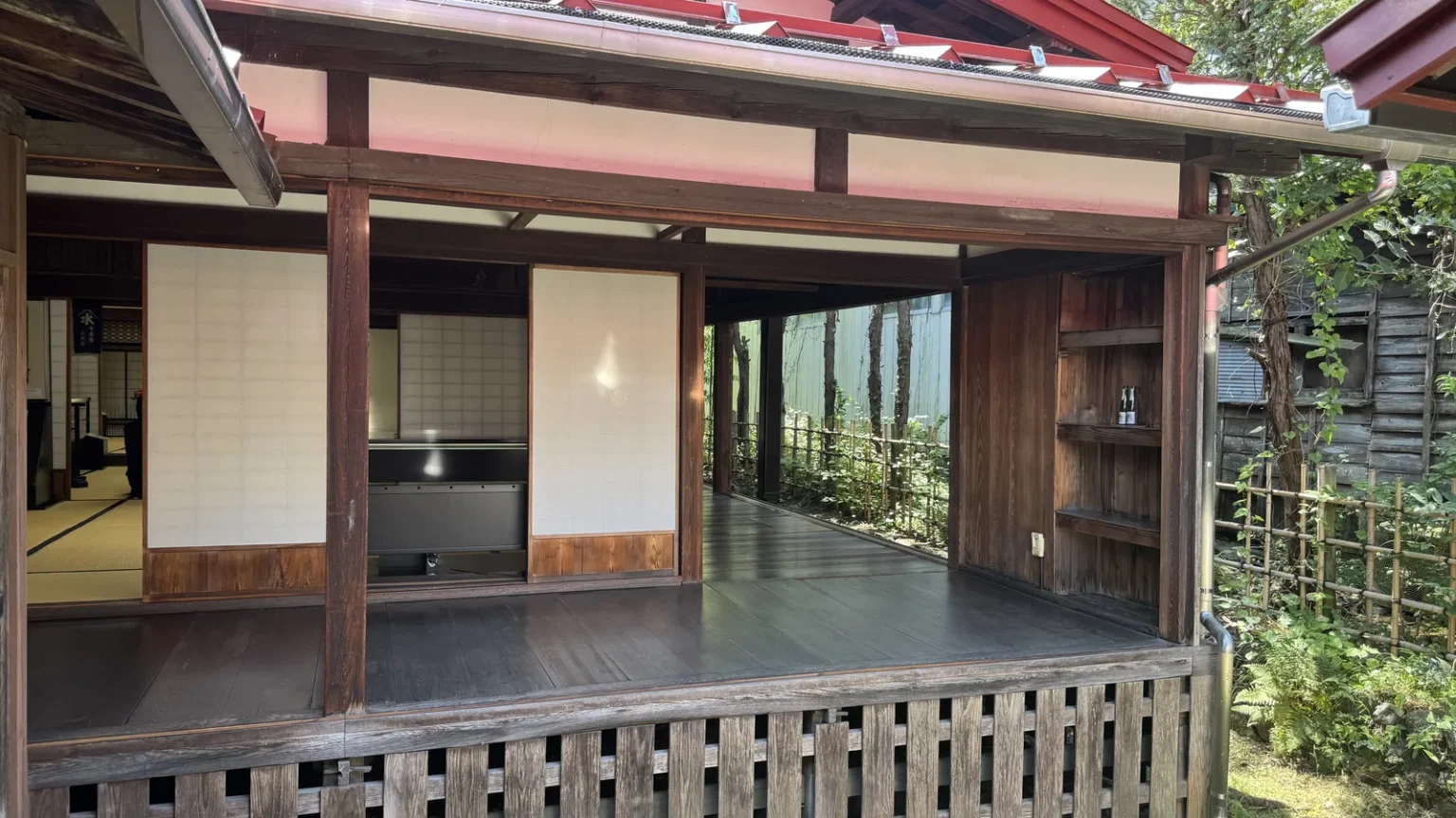 A raised wooden veranda and tatami rooms with paper screens, seen from the garden side under a red roof