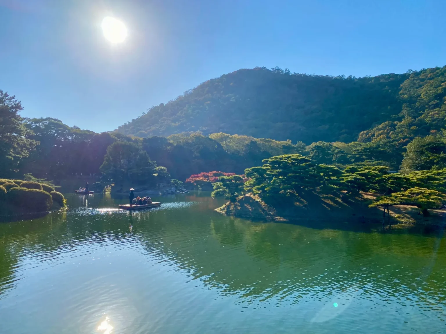 A wooden boat on the South Pond of Ritsurin Garden, below a wooded hill