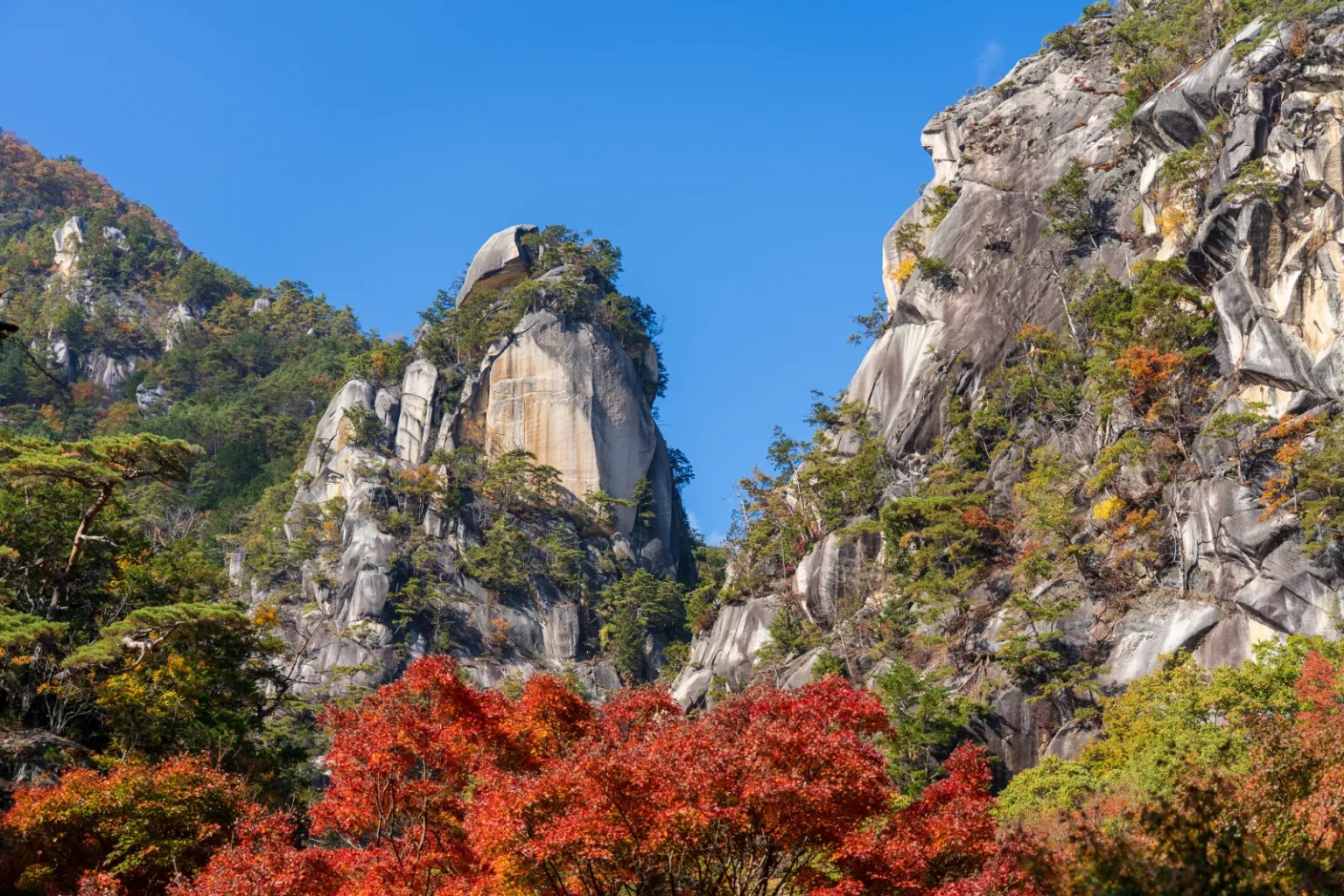 A tall pale rock peak under a blue sky, with red autumn foliage below