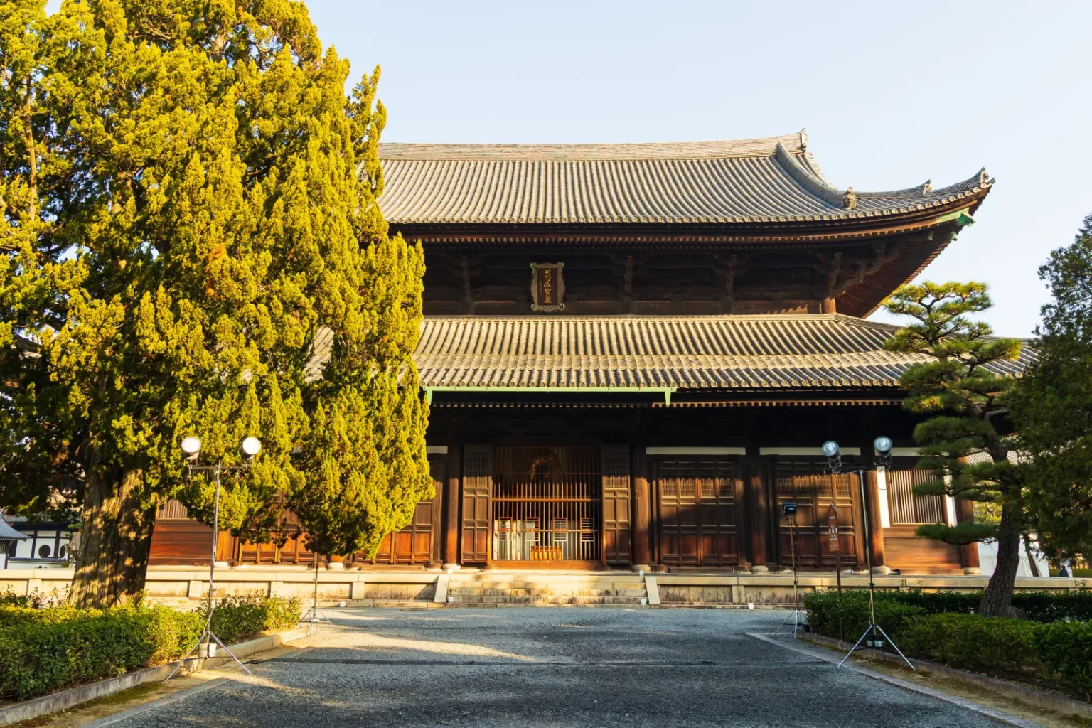 The main hall of Tofukuji, a large two-storey wooden building with grey tiled roofs, across a paved courtyard with trees on the left