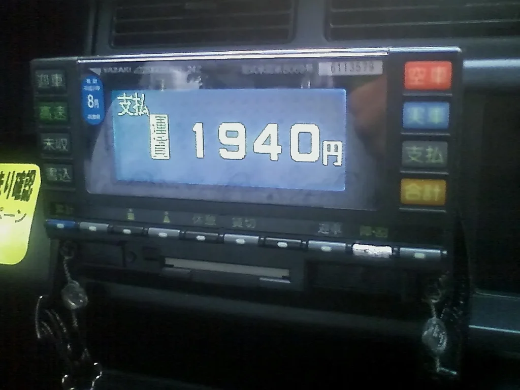An older taxi meter on a dashboard showing a fare of 1,940 yen on its display, with buttons labelled in Japanese around it