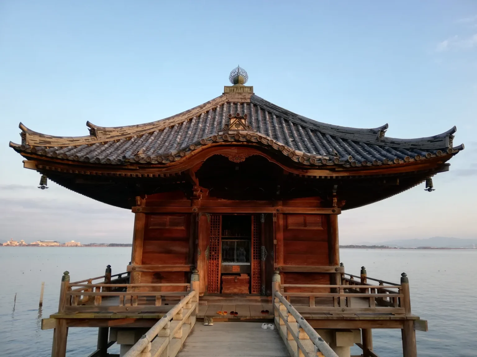 The wooden Ukimido hall with a curved tiled roof standing on pillars in Lake Biwa, reached by a short bridge, in late-afternoon light