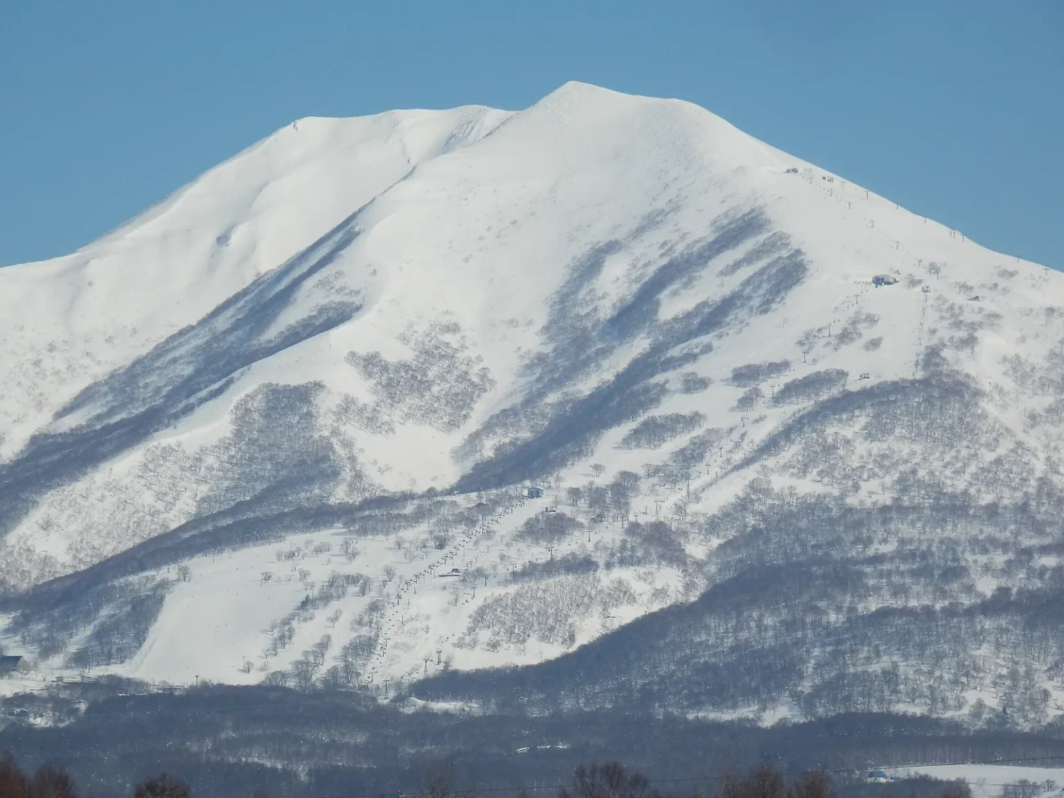 The snow-covered peak of Niseko Annupuri under a blue sky, with ski runs on its lower slopes, seen from Satomi in Niseko town