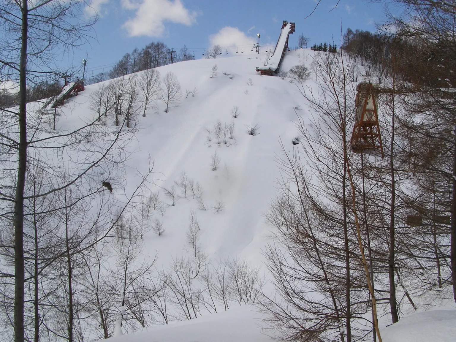 A snow-covered slope with a ski jump tower at the top and bare trees in front, at Asahigaoka in Kutchan town
