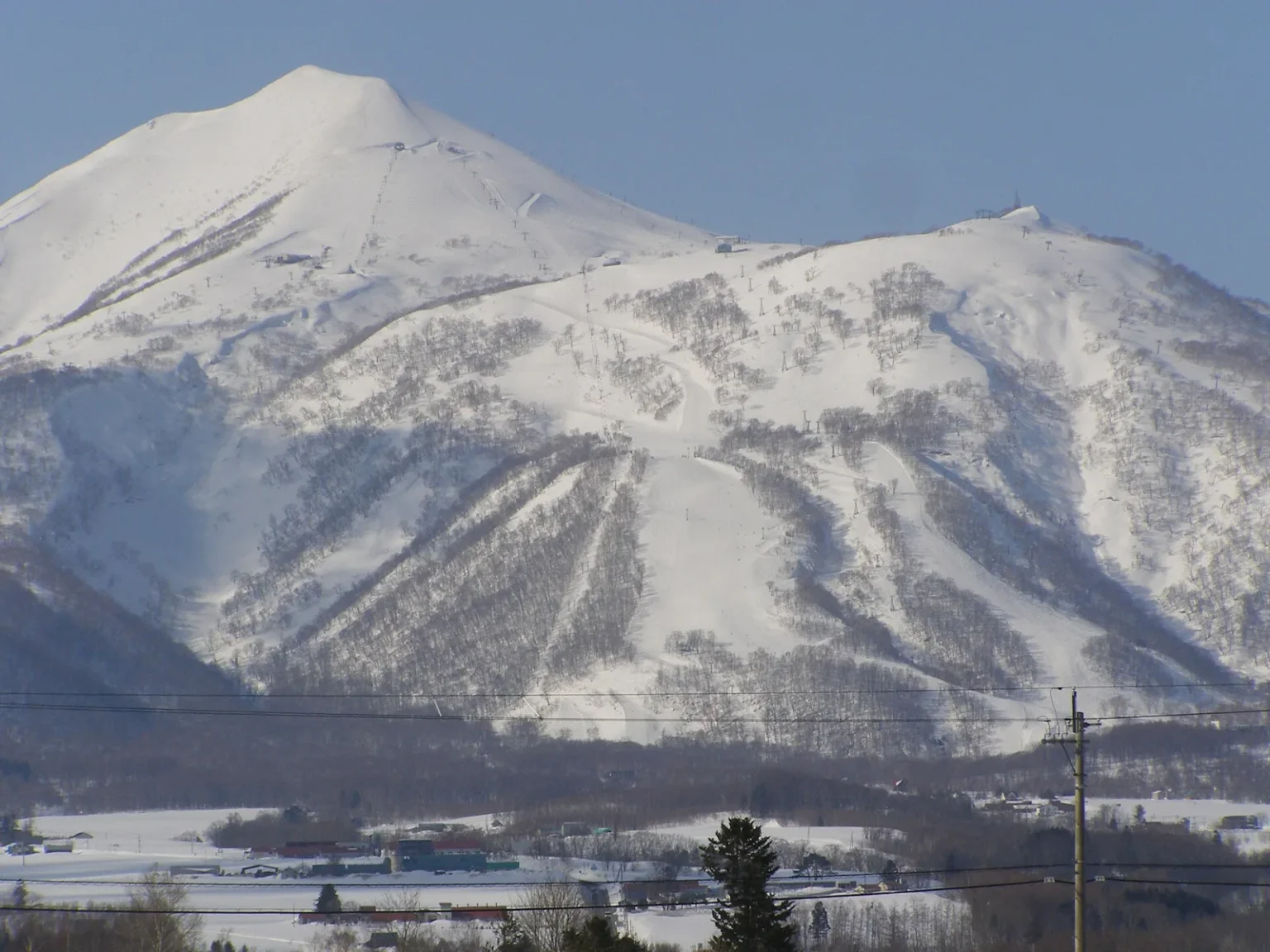 The snow-covered eastern slopes of Niseko Annupuri above the Higashiyama area, with ski runs cut through the trees, seen from Satomi in Niseko town