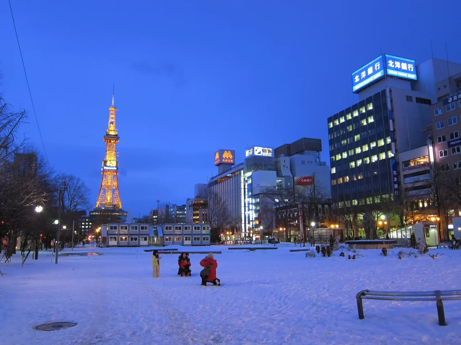 Snow-covered Odori Park at dusk with the lit Sapporo TV Tower and office buildings
