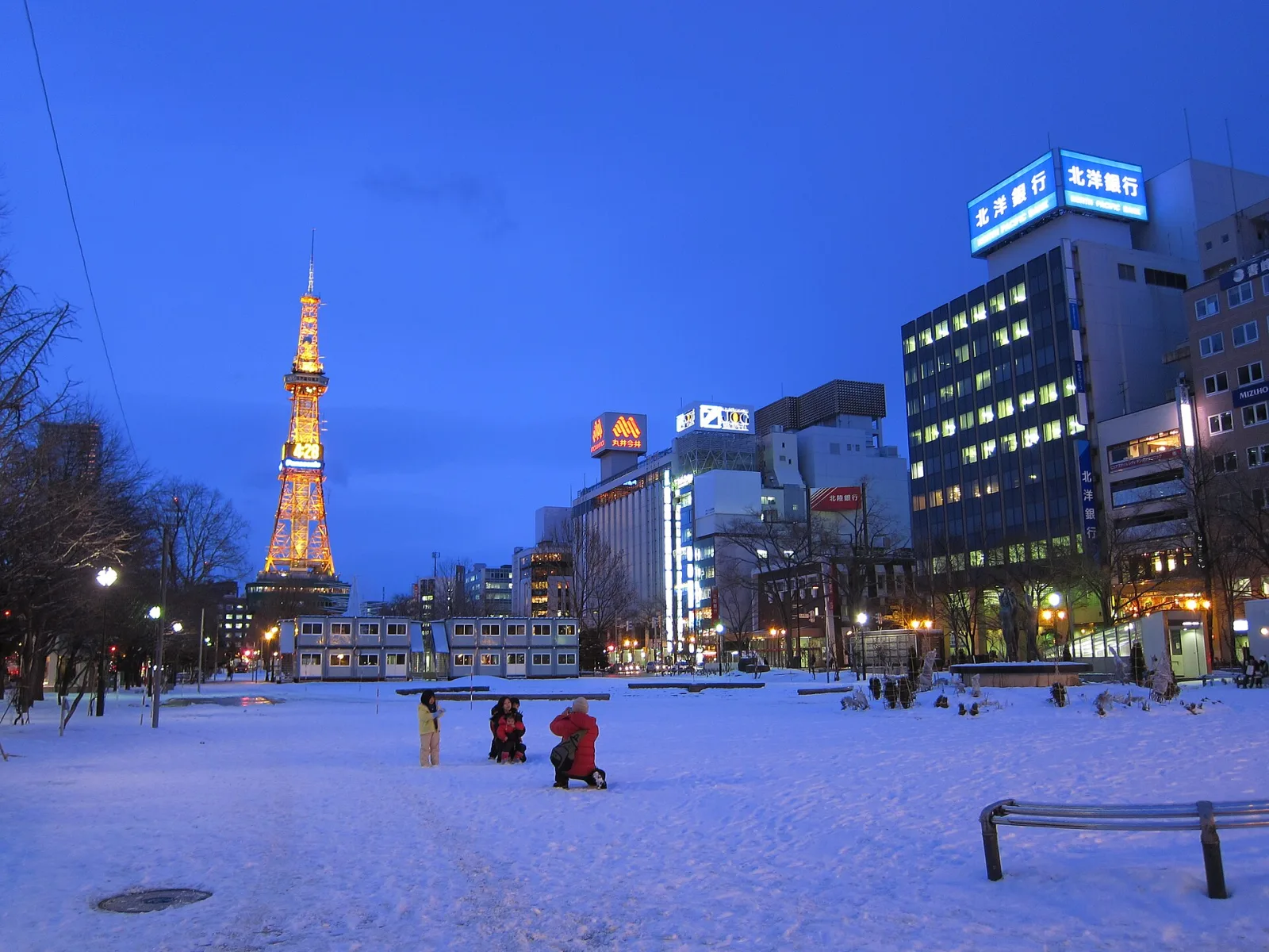 Snow-covered Odori Park at dusk with the lit Sapporo TV Tower on the left and office buildings on the right