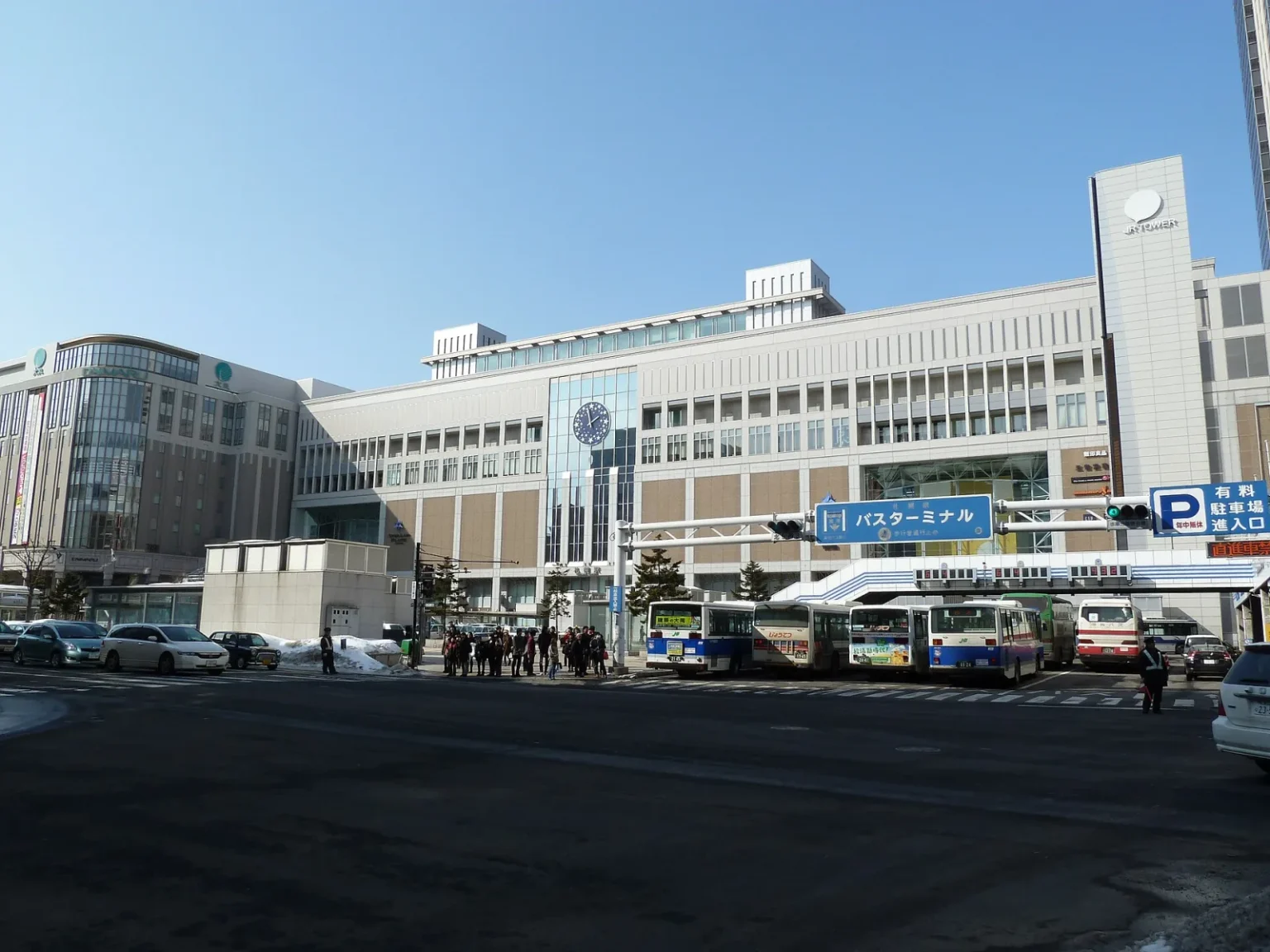 The south side of JR Sapporo Station with the JR Tower sign, a clock on the facade and buses at the bus terminal in front