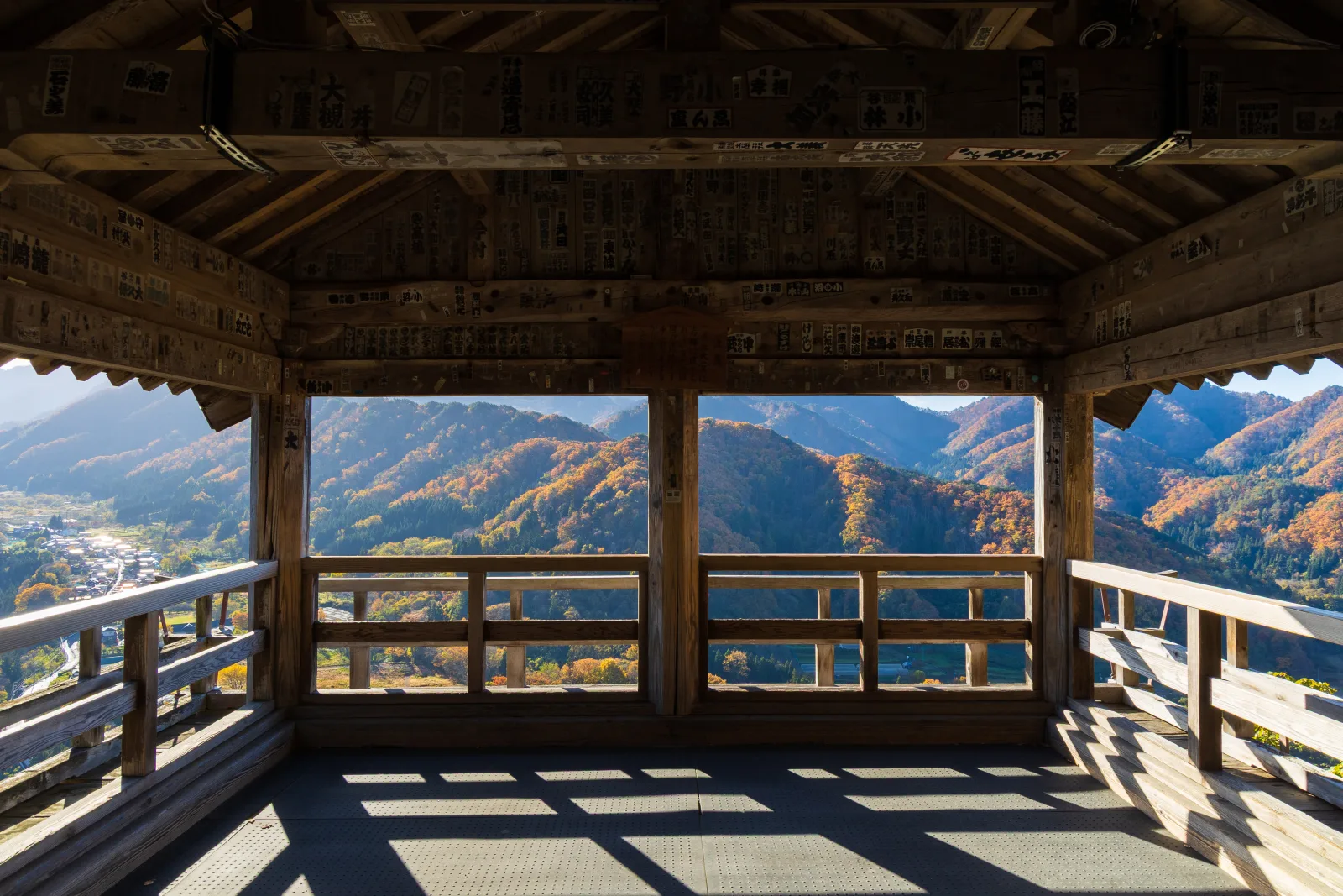 The view from inside the wooden Godaido hall at Yamadera, looking out between its pillars over mountains in red and orange autumn colour and the village in the valley